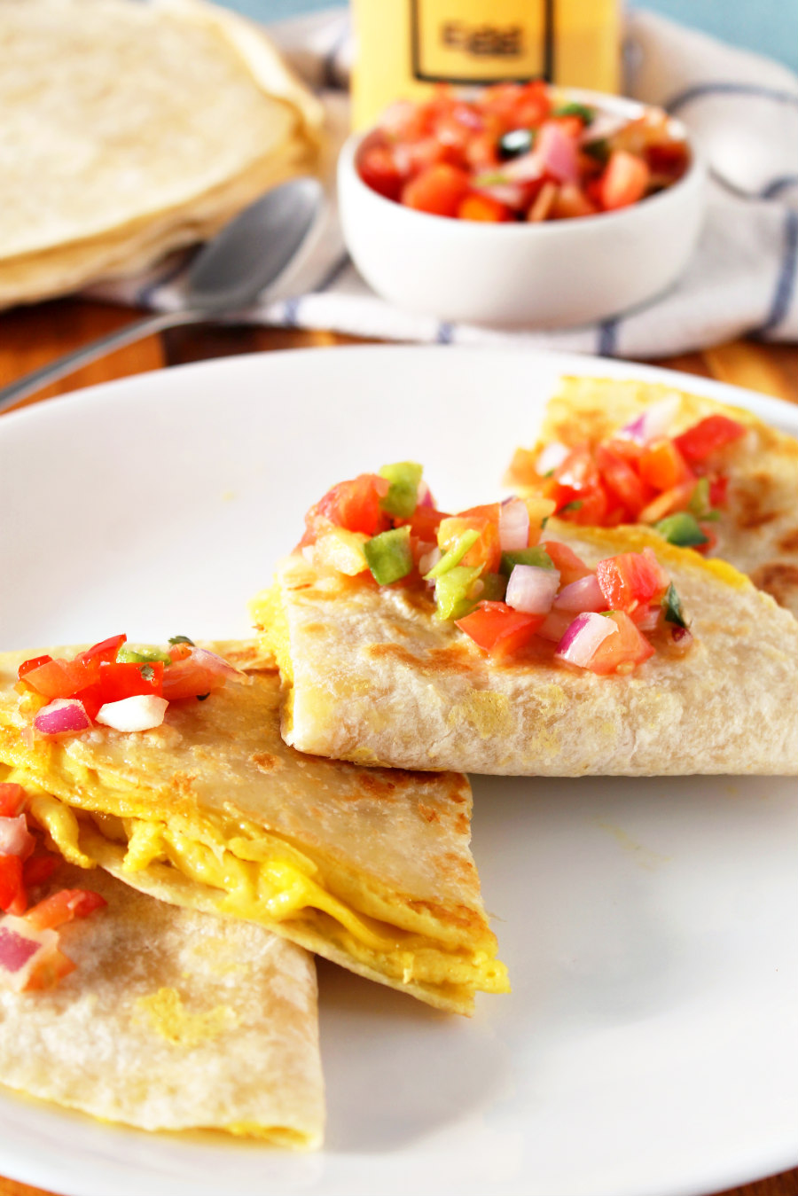 Easy Vegan Breakfast Quesadillas stacked with fresh salsa on top. Bowl of fresh salsa, spoon, Just Egg container, and tortillas in the background.