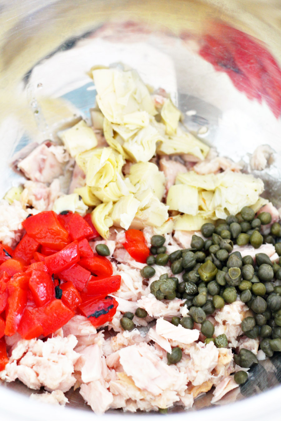 Canned tuna, roasted red peppers, marinated artichokes, and capers in a mixing bowl.