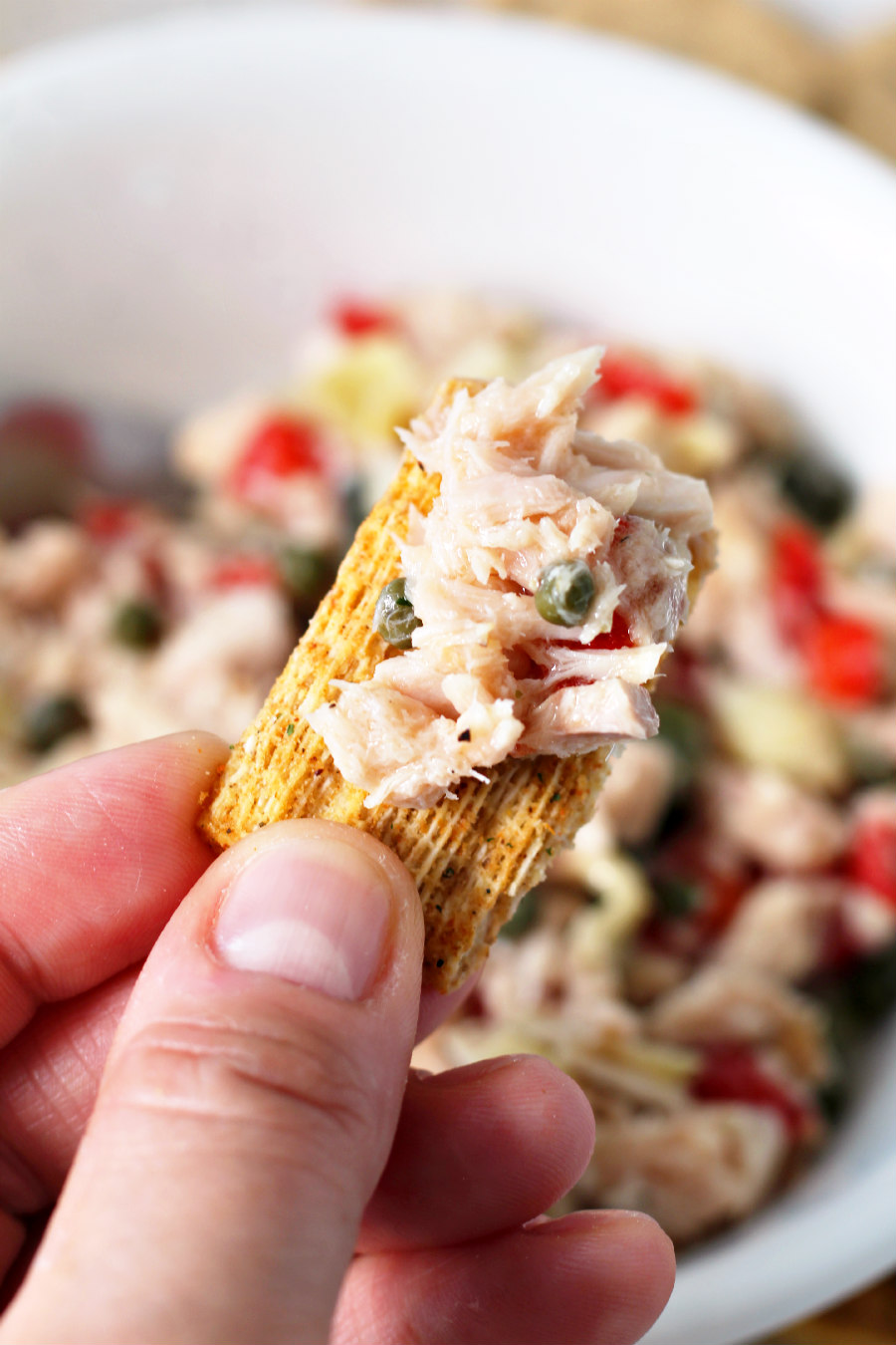 Hand holding Triscuit cracker topped with Mediterranean Tuna Salad.
