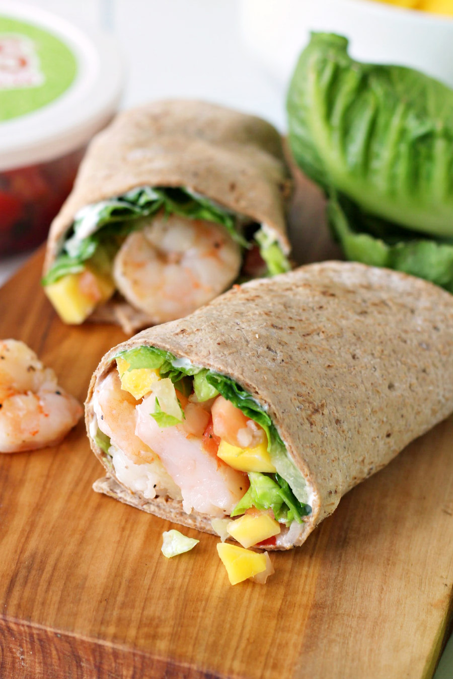 Island Mango and Shrimp Wrap on a wooden board. Ingredients in the background.