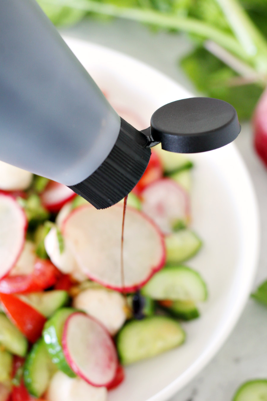 Balsamic glaze being drizzled over the top of Tomato, Cucumber, and Radish Salad.