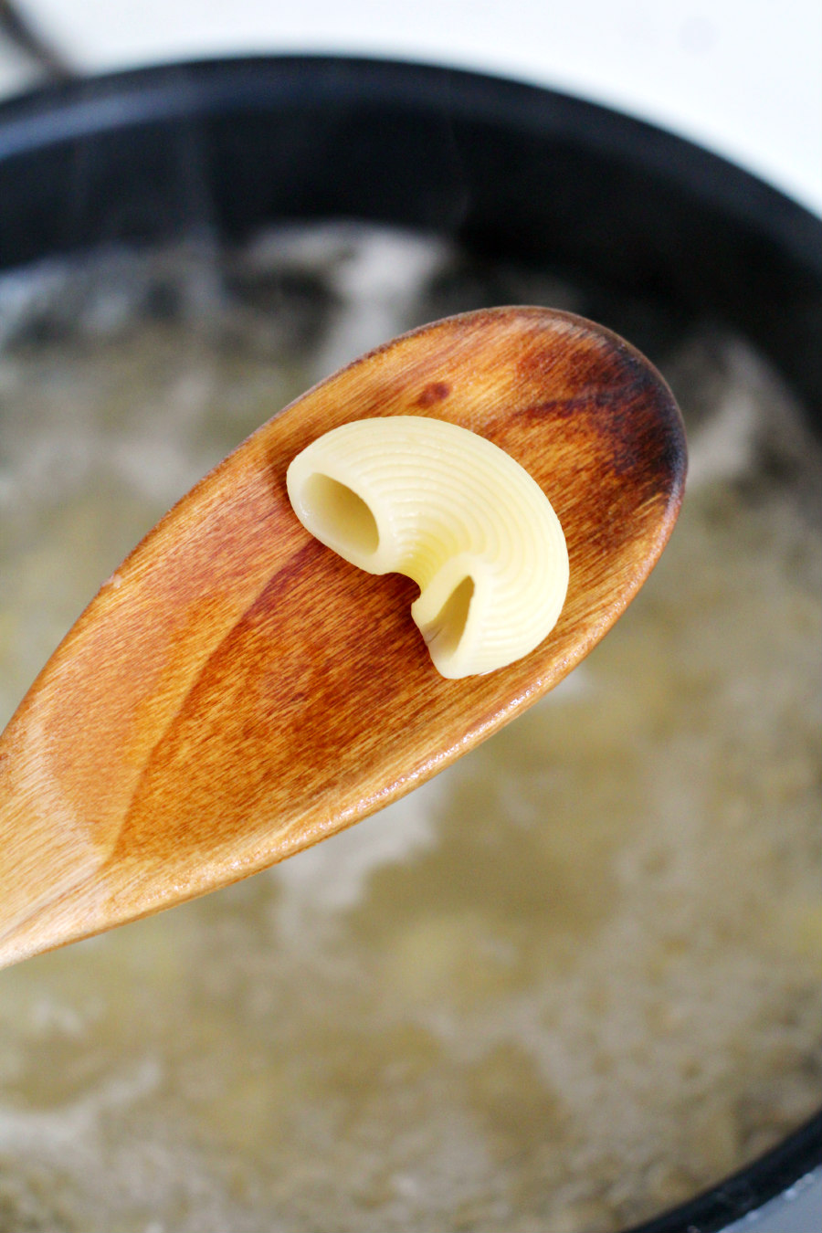 Wooden spoon holding up chiocciole pasta over a pot of boiling water.