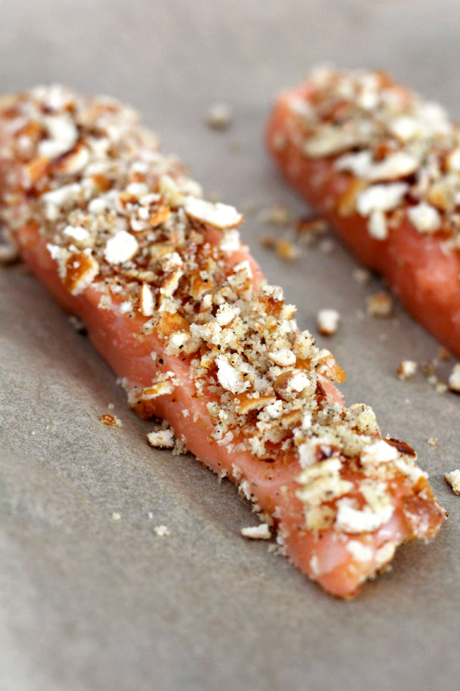 Raw salmon on a parchment lined baking sheet crusted with crushed lemon pepper pretzels.
