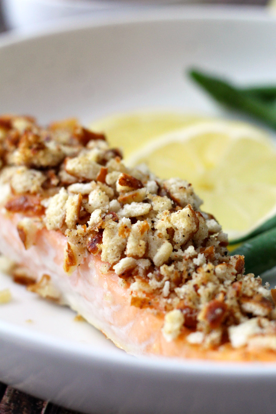 Close up of Lemon Pepper Pretzel Crusted Salmon plated with lemon slices and sauteed green beans.