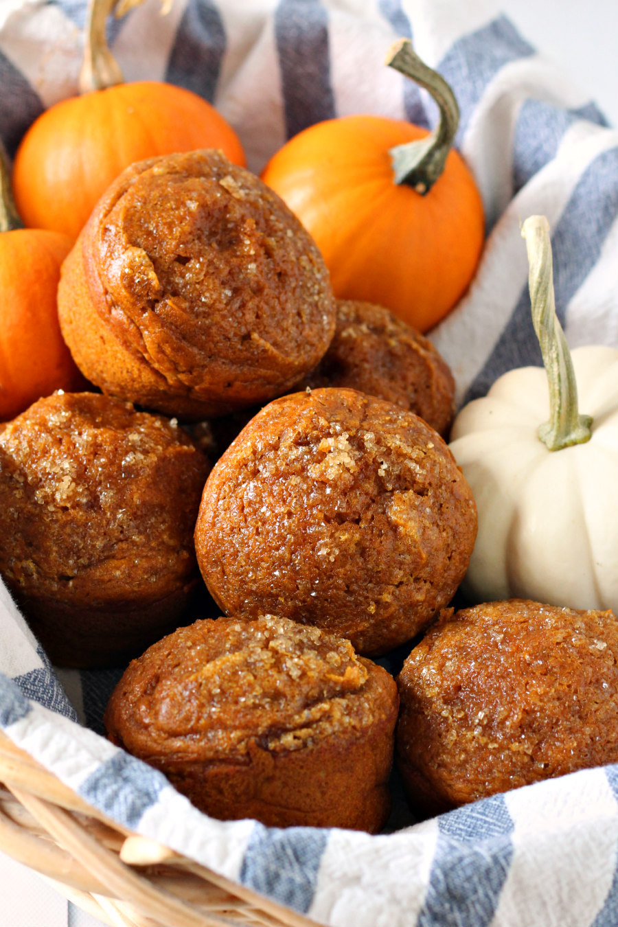 Bakery Style Pumpkin Muffins in striped towel lined basket with mini pumpkins.