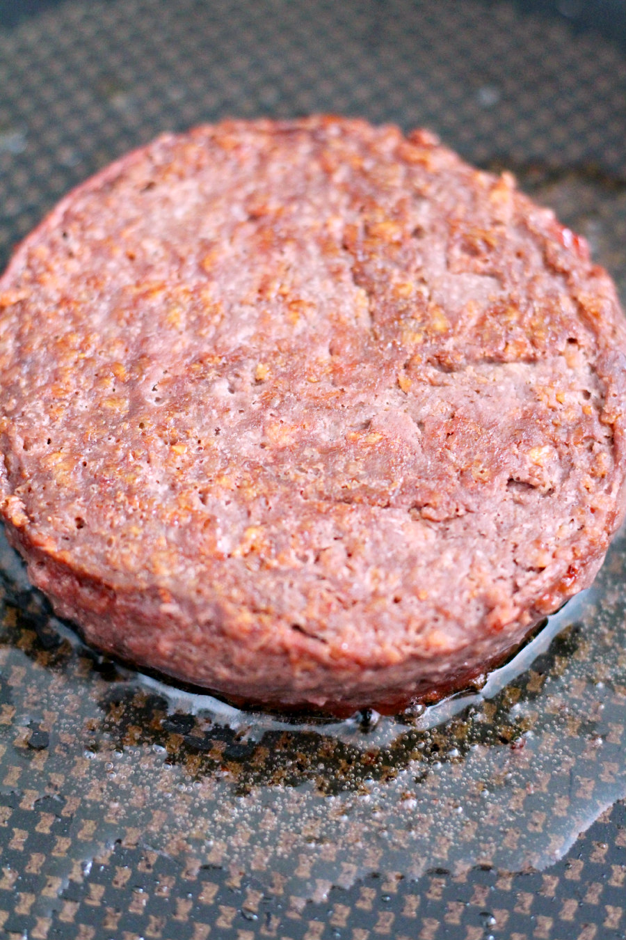 Plant based burger patty being cooked in a skillet.