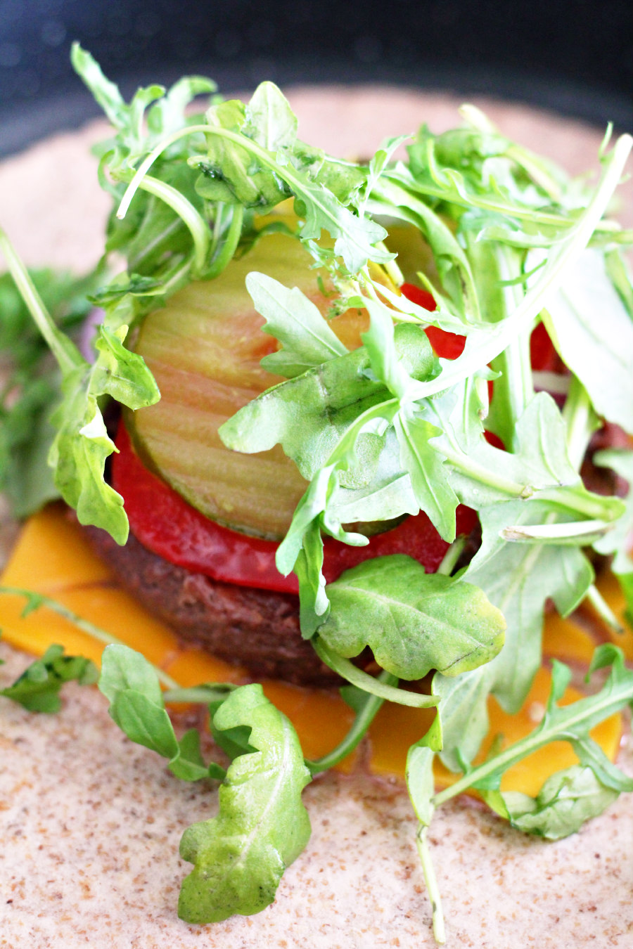Soft tortilla in skillet topped with plant based cheese, plant based burger patty, tomato, onion, pickles, and arugula.