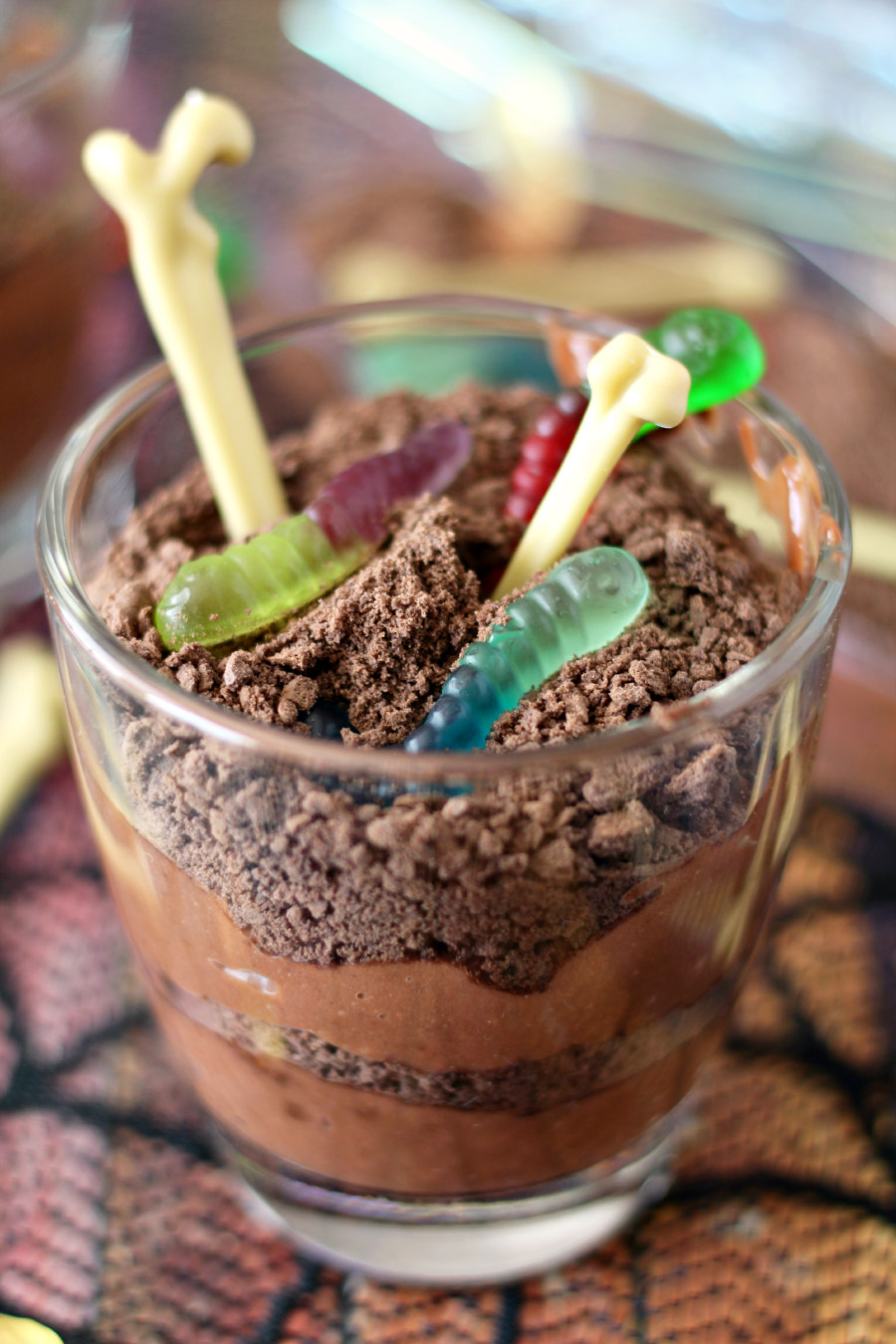 Glass of Dirt and Worm Chocolate Pudding topped with gummy worms and plastic bones.