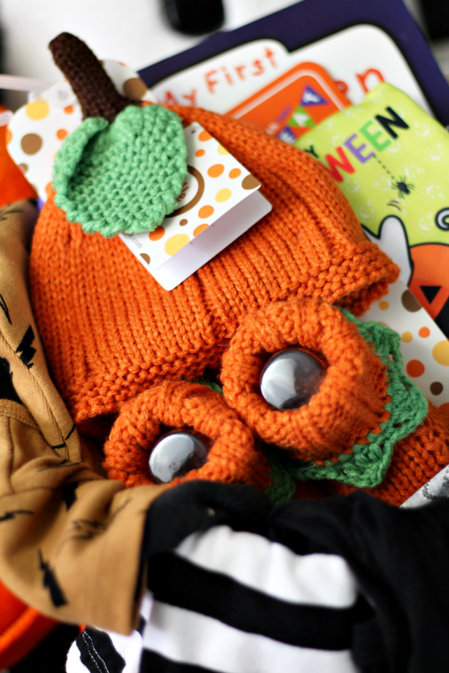 Close up photo of Baby's First Halloween gift basket including knit pumpkin hat and booties, books, and clothes.
