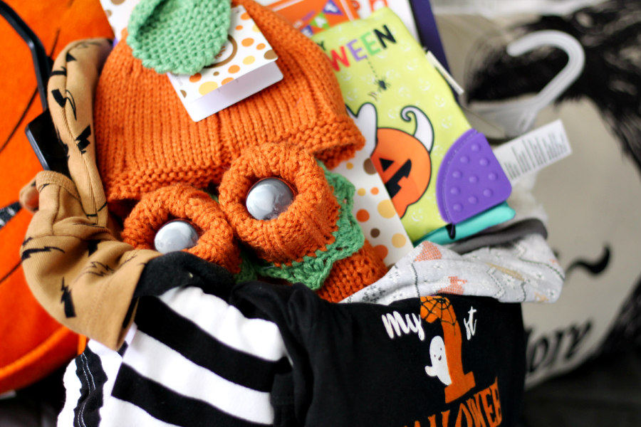 Horizontal photo of knit hat and booties, clothes, and books in Halloween bucket.