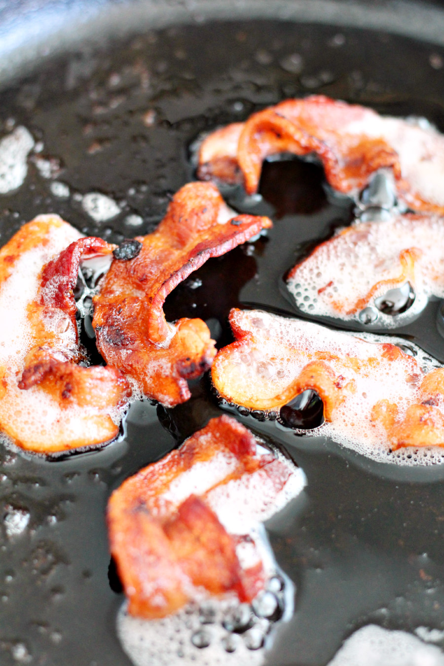 Strips of bacon being cooked in a cast iron skillet.