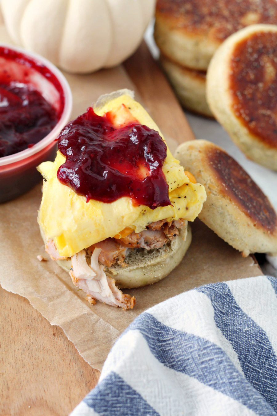 Thanksgiving Leftovers Breakfast Sandwich opened with cranberry sauce spooned on top. Muffins, white pumpkin, and cranberry sauce container sit in background.