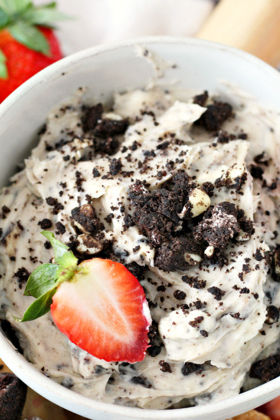 Close up of Cookies and Cream Cheese Dip in bowl with sliced strawberry. Strawberries can be seen in background.
